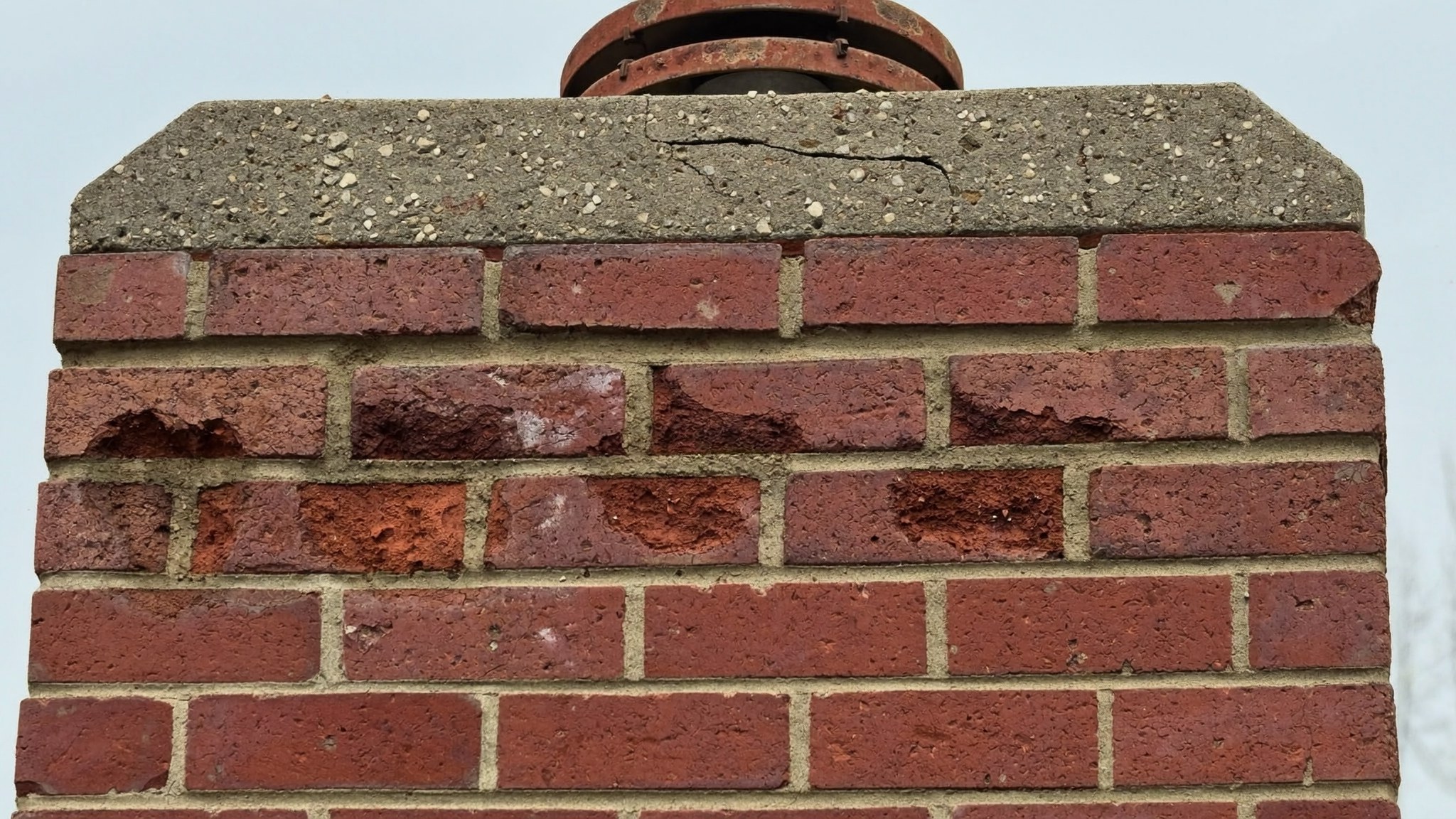 Spalled brick faces, eroded mortar joints and a cracked concrete crown on a Rowlett, TX chimney needing repair