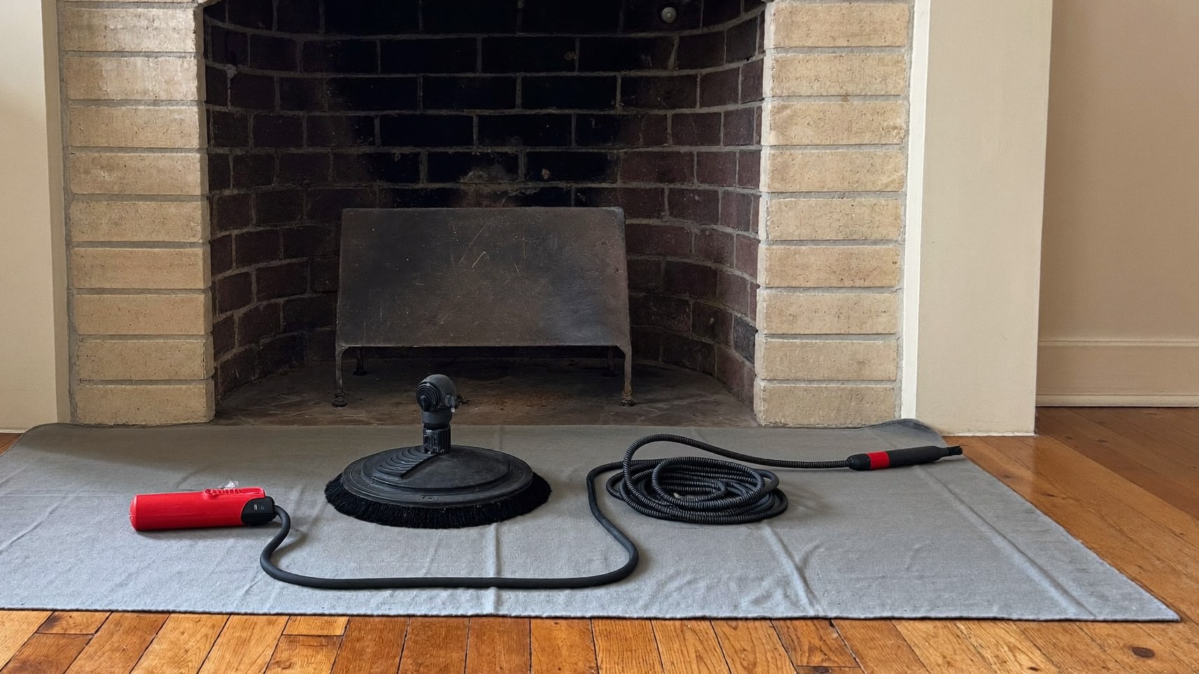 Rotary chimney sweep brush and drive rod on a drop cloth in front of a masonry firebox during a chimney sweep in Grapevine TX